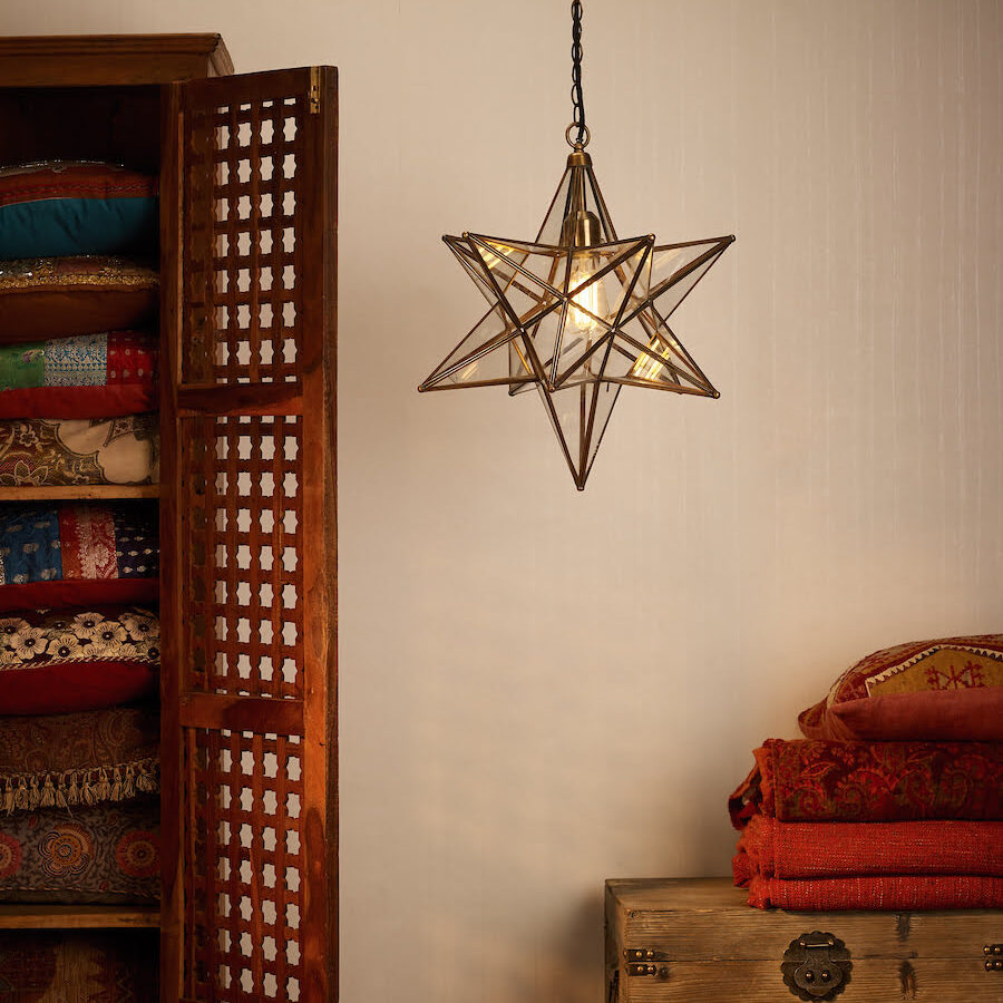 Ilario Star-shaped Pendant Light in Antique Brass & Glass next to an Eastern-style cupboard filled with cushions